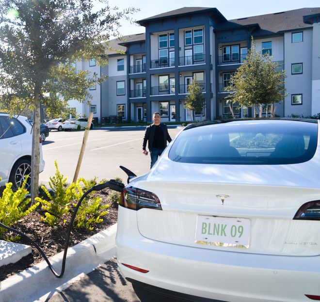 Valkoinen Tesla latauksessa kerrostalon parkkipaikalla.